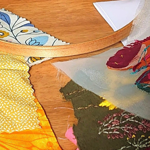 A table littered with embroidery materials, including fabric scraps, thread, and embroidery hoops.