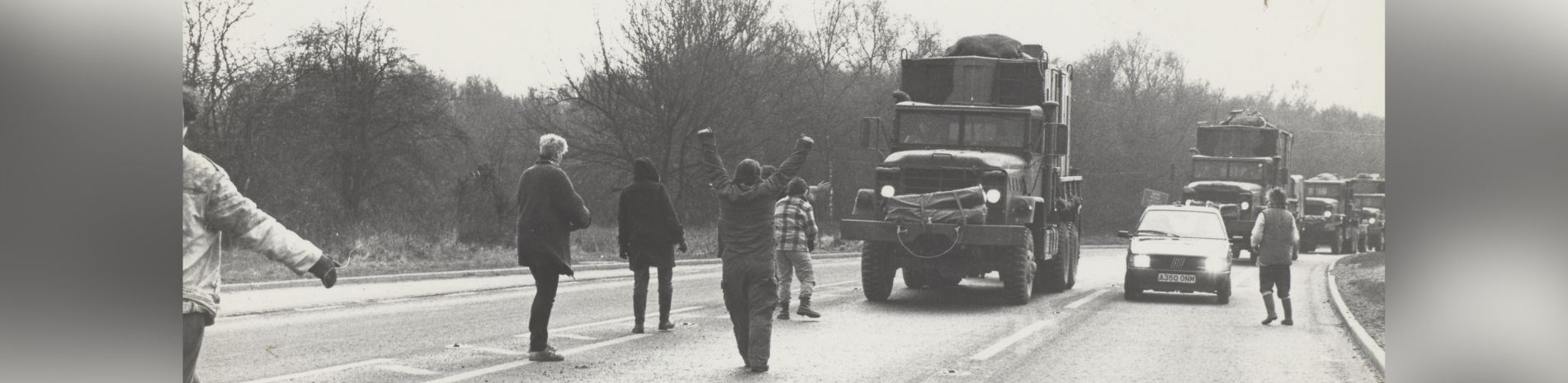 Women standing on the road in front of a military convoy.