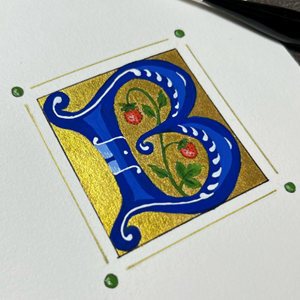 A repeated image of an illuminated letter, ‘B’, in deep blue with gold embellishments. A paintbrush rests above the paper.