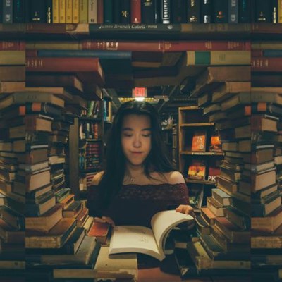 A woman looks through a circle-shaped gap in a wall of books.