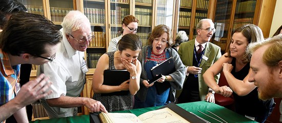 People standing around a music manuscript looking excited and pointing at it.
